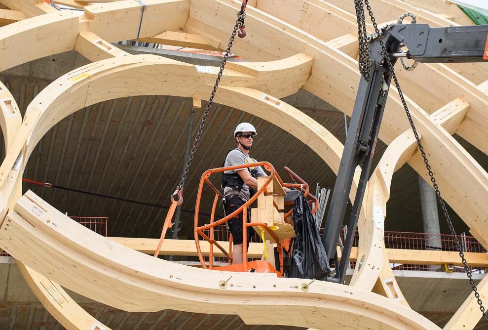 Un monteur avec une grue de levage orange se trouve au milieu de la construction en bois du bâtiment Swatch